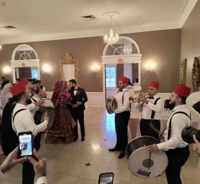 A traditional wedding celebration with musicians wearing red fezzes and a bride in ornate attire Dabke Group