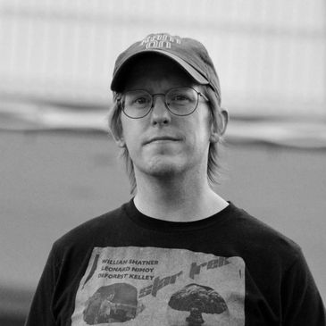Man wearing glasses, blue cap, and black graphic t-shirt.