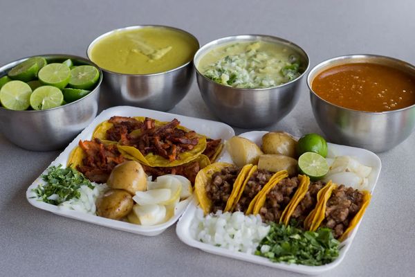 Plates of tacos with various toppings and sides including lime and sauces.