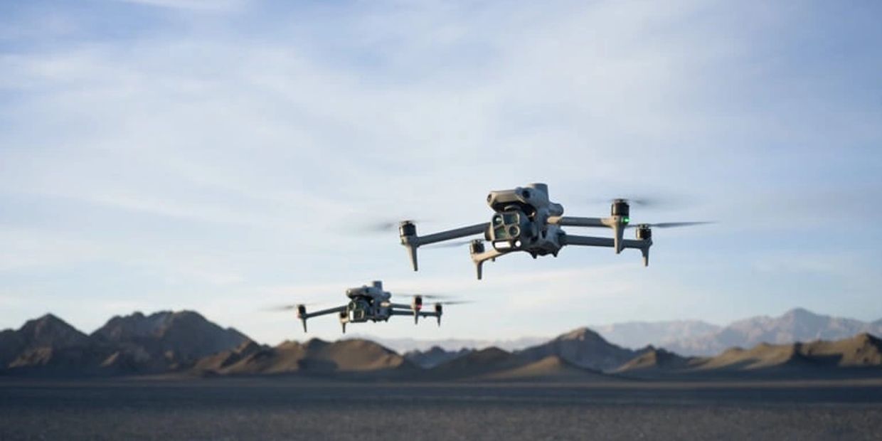Two drones flying over a desert landscape with mountains in the background.