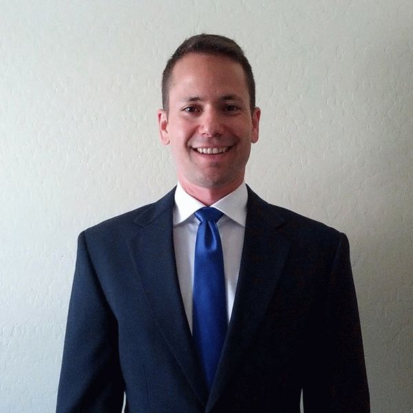 Man in a dark suit with a blue tie smiling at the camera.