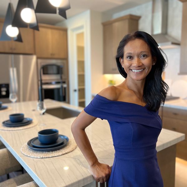 Woman in a blue dress smiling in a modern kitchen.