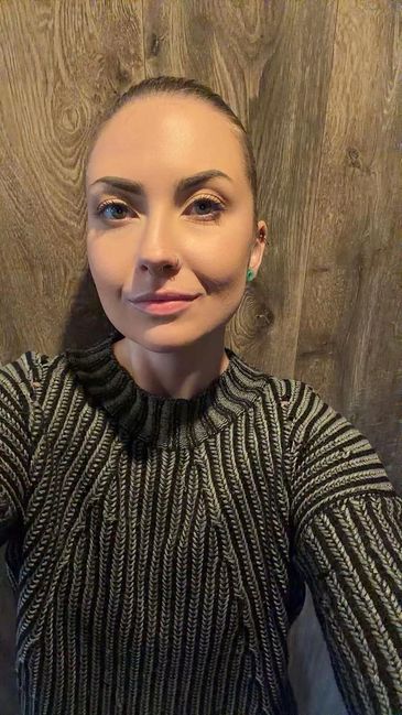 Woman with neatly pulled-back hair wearing a striped sweater against a wooden background.