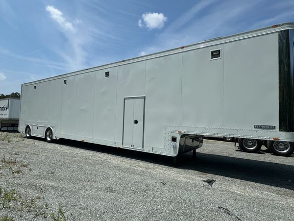 A large white trailer parked on gravel under a partly cloudy sky.