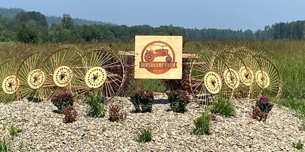 Farm sign surrounded by vintage machinery wheels and plants.