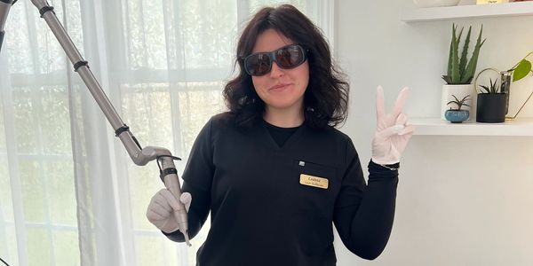 Woman in black with sunglasses holding a dental tool and making a peace sign.