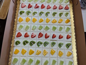A large tray of neatly arranged fruit-topped cream squares.