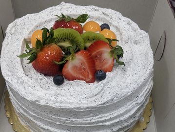 A round cake topped with strawberries, kiwi, blueberries, and melon balls with speckled white frosting.