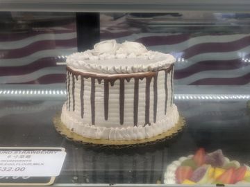 Round white cake with chocolate drips and floral frosting decoration.