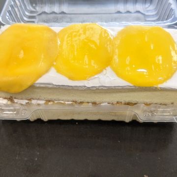 A slice of cake with white frosting and three yellow fruit slices on top.
