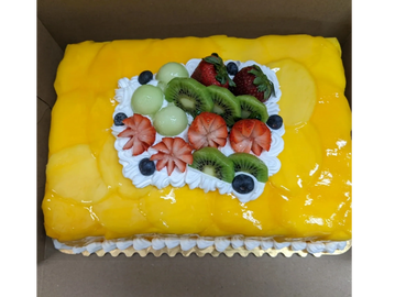 A rectangular mango-topped cake decorated with strawberries, kiwi, blueberries, and melon balls.