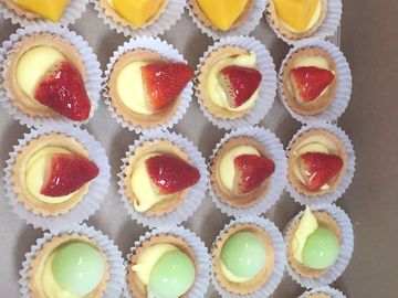 Assorted mini fruit tarts with mango, strawberry, and green grape toppings.