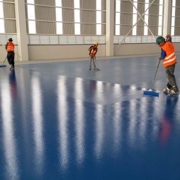 Trabajadores limpiando o pintando un piso azul.