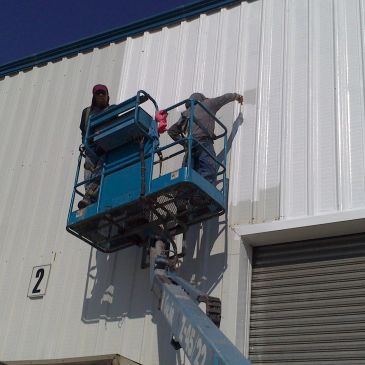 Dos personas pintan una pared con una plataforma elevadora.