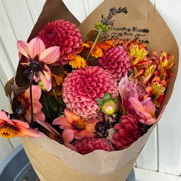 A colorful bouquet of pink, orange, and yellow flowers wrapped in brown paper.