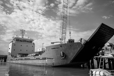 Large cargo ship docked with ramp lowered and crane overhead.