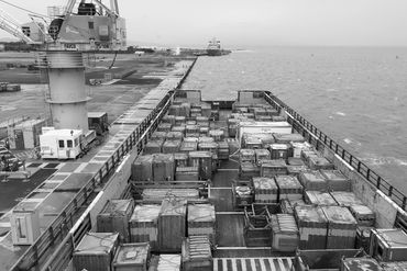 A cargo ship loaded with containers docked at a port with a crane.