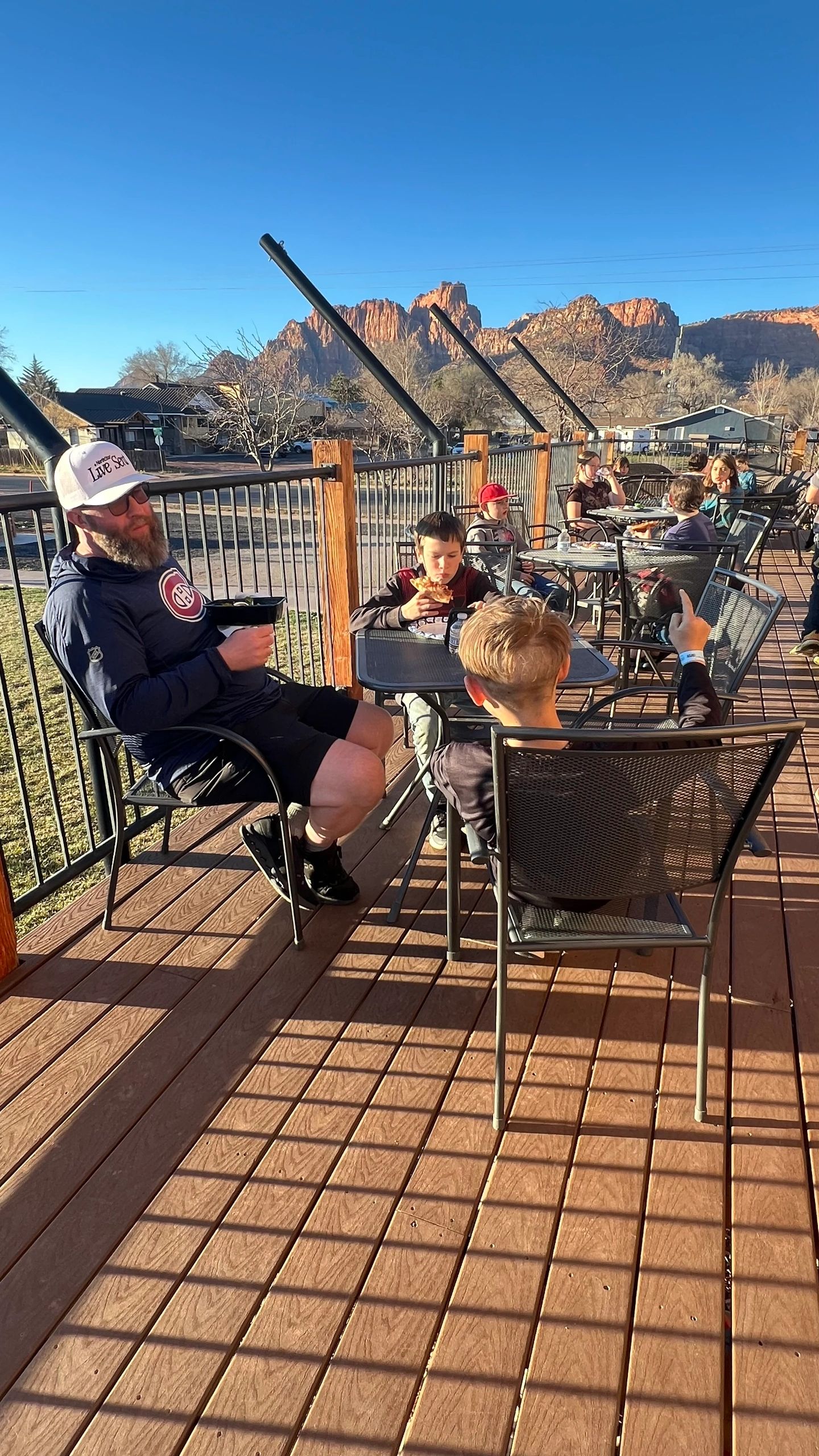 People enjoy outdoor dining on a sunny patio with mountain views.