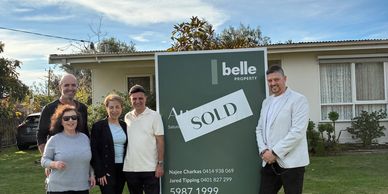 Group of people standing around a sold real estate sign.