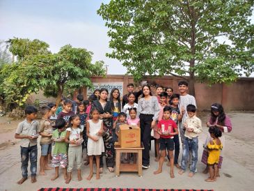 Group of children and young adults outdoors with a cardboard box on a table.