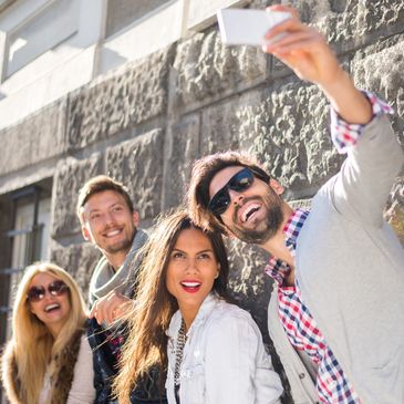 Two couples vacationing, around 40 years old, take a selfie with a brick wall in the background.