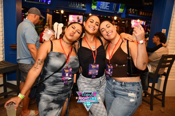 Three friends smiling and posing at a nightlife cocktail crawl event.