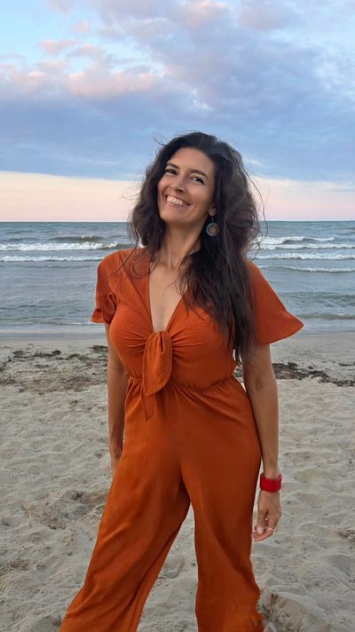 Woman smiling on the beach in an orange outfit.