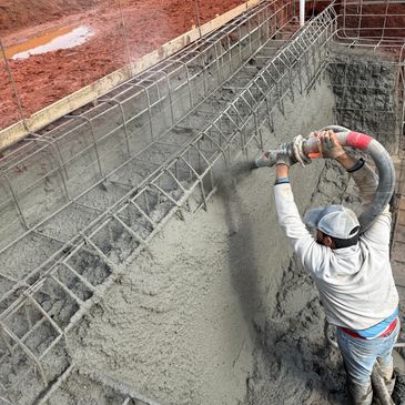 Worker spraying concrete inside a rebar structure at a construction site.