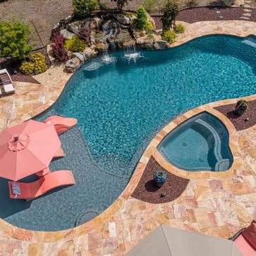 A luxurious backyard pool with waterfall, slide, and shaded lounge chairs.