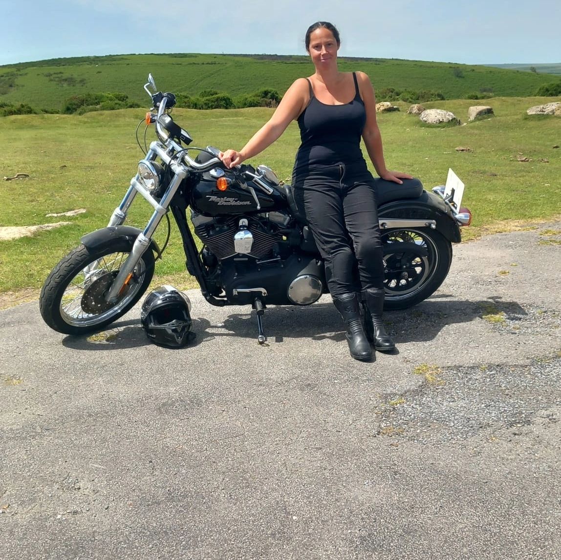 Woman sitting on a black Harley-Davidson motorcycle outdoors.