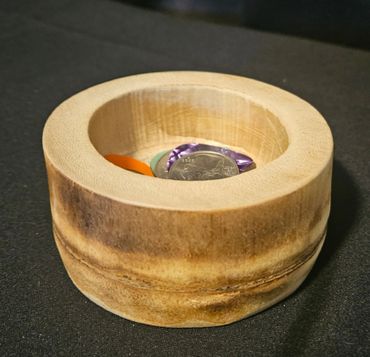 A wooden bowl holding guitar picks and a coin on a dark surface.
