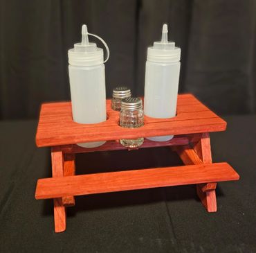 Miniature picnic table holding condiment bottles and shakers.
