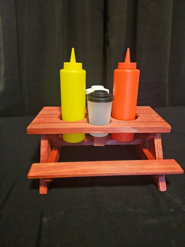 Miniature wooden picnic table condiment holder with yellow and orange squeeze bottles.