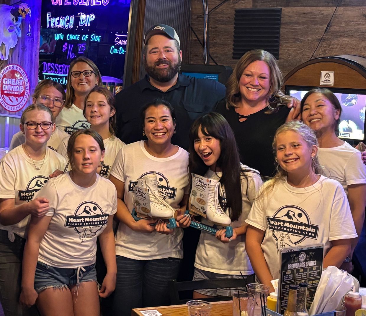 Group photo of happy figure skaters and coaches holding trophies.