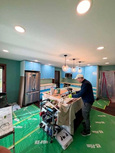 A man working on kitchen renovation surrounded by tools and protective floor covering.