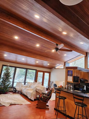 Cozy living room with wooden ceiling, Christmas tree, and furniture covered in white sheets.