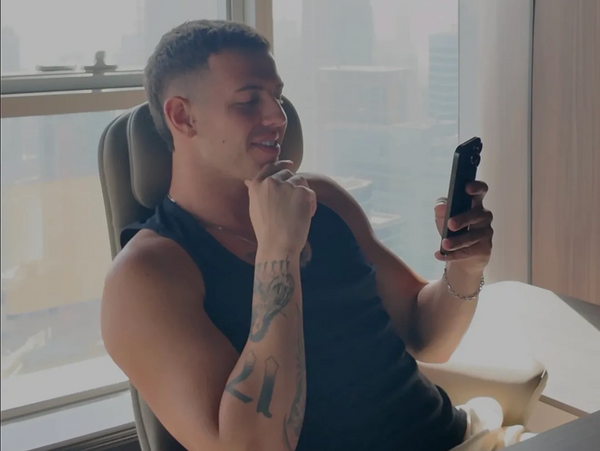 Man in black tank top sitting, looking at phone with smile.