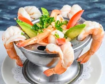 Shrimp cocktail served in a metal bowl with avocado and garnish.