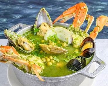 A pot of green seafood soup with crab, clams, and mussels.