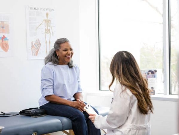 A doctor smiling and talking to a female patient in a medical office.