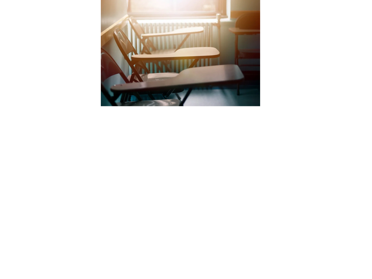 Photo of 3 empty school desks in front of a classroom window