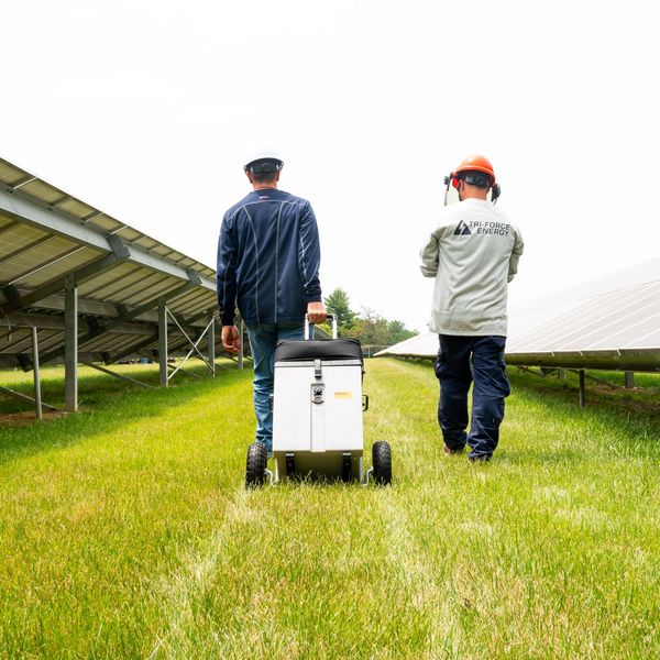 Certified Solar Technicians walking testing equipment through solar panel array.
