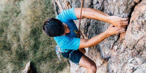 Man rock climbing on a steep cliff with safety rope.