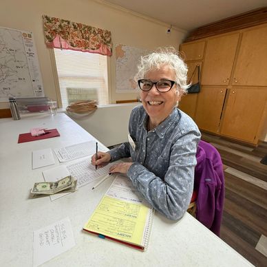 Smiling elderly woman writing at a table with papers and money.