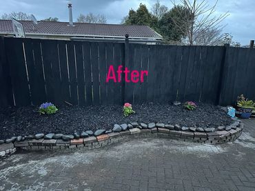 Newly landscaped garden bed with dark mulch and flowers against a black fence.