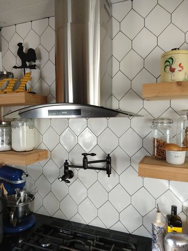 white tile backsplash in kitchen with floating shelves with a glass and stainless steel vent hood