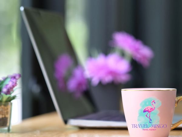 Laptop, flowers, and a Travel-Mingo mug, prepared for a travel agency proposal review meeting.