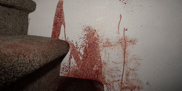 Blood splattered on a white wall beside carpeted stairs.