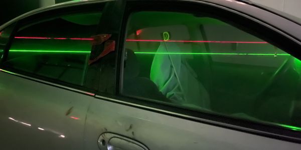 Green and red laser beams crossing a car door window.