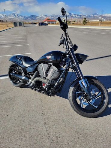 Black custom motorcycle parked in an empty lot with mountains in the background.